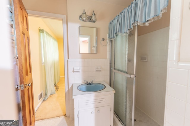 bathroom featuring wainscoting, a shower stall, tile walls, vanity, and visible vents