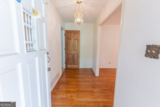 hall with light wood-style floors and a notable chandelier