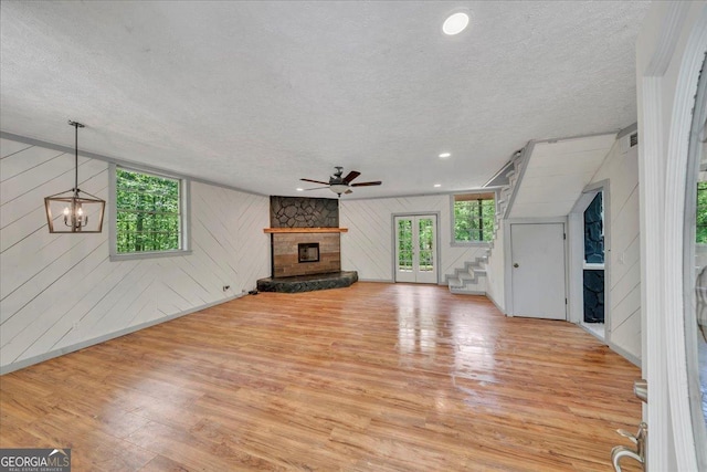 376 Mauldin Rd, Thomaston, GA 30286 - unfurnished living room featuring stairs, ceiling fan, a stone fireplace, light wood finished floors, and a textured ceiling