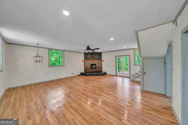 376 Mauldin Rd, Thomaston, GA 30286 - unfurnished living room with light wood-style floors, wood walls, ceiling fan, a stone fireplace, and a textured ceiling