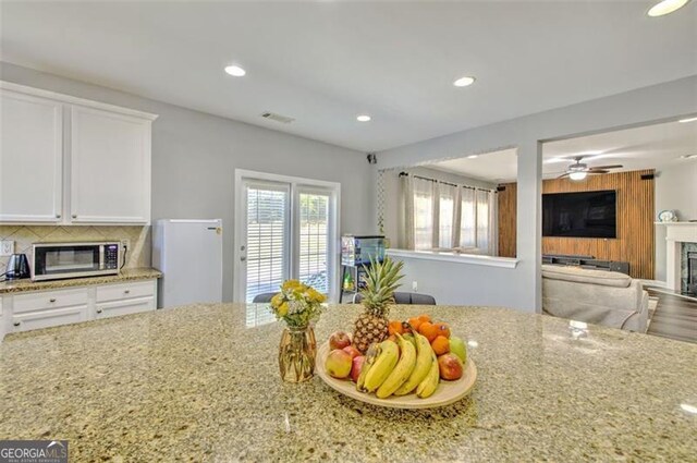 5845 Princeton Run Trl, Tucker, GA 30084 - kitchen with stainless steel microwave, a glass covered fireplace, light stone counters, white cabinetry, and recessed lighting