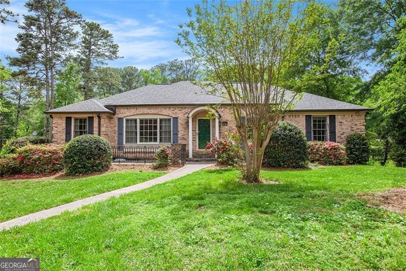 ranch-style home featuring roof with shingles, a front yard, and brick siding
