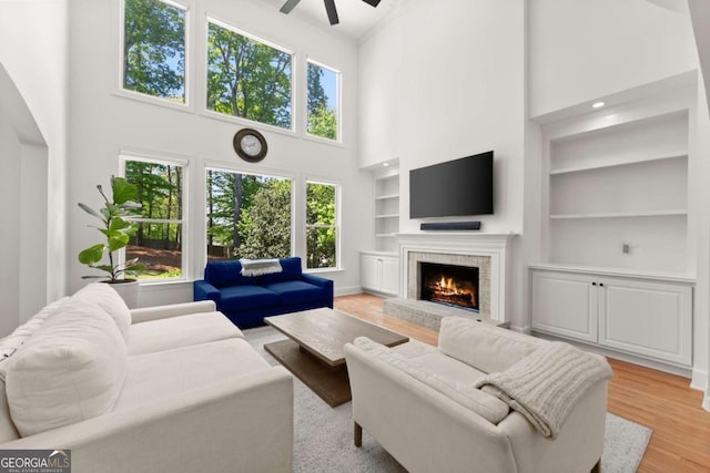 living room featuring a brick fireplace, a towering ceiling, a wealth of natural light, and built in shelves