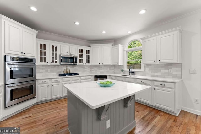 kitchen with appliances with stainless steel finishes, a sink, light countertops, white cabinetry, and light wood-type flooring