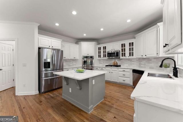 kitchen with decorative backsplash, appliances with stainless steel finishes, a center island, a sink, and white cabinetry