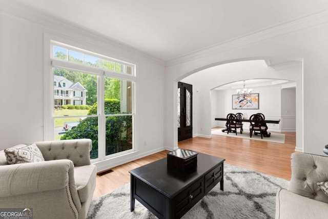living room with crown molding, a notable chandelier, arched walkways, wood finished floors, and visible vents