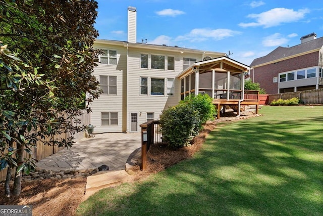 rear view of property with fence, a patio, a chimney, a sunroom, and a lawn