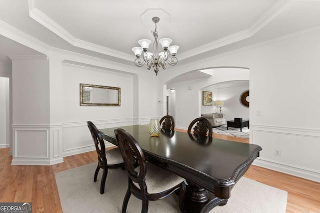 dining area with crown molding, arched walkways, an inviting chandelier, and light wood-style flooring
