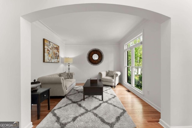 living room with arched walkways, baseboards, ornamental molding, and wood finished floors