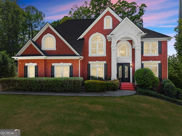 view of front of property with french doors, brick siding, and a front yard
