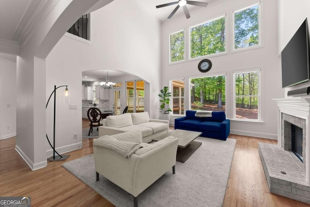 living room featuring ornamental molding, a fireplace, baseboards, light wood-type flooring, and arched walkways