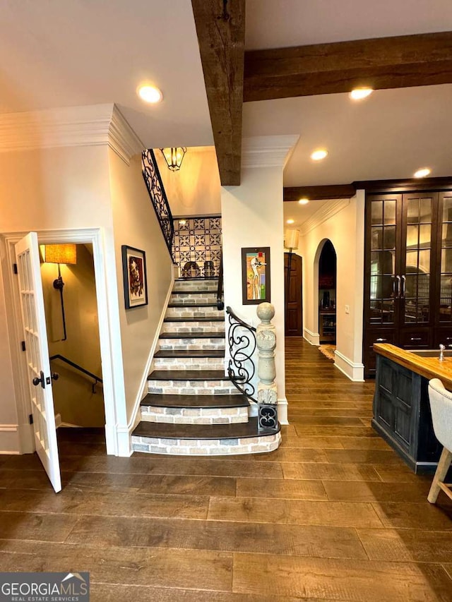 stairway with crown molding, baseboards, wood-type flooring, and arched walkways