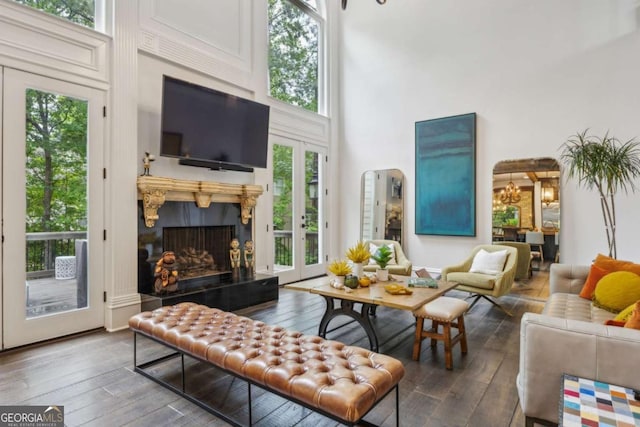 living room with arched walkways, a premium fireplace, wood-type flooring, a notable chandelier, and a towering ceiling