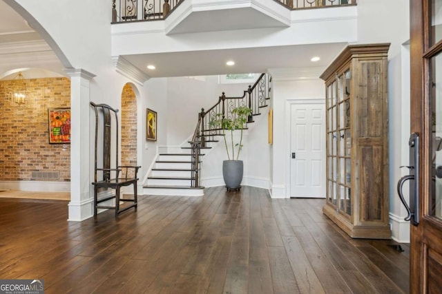entrance foyer featuring dark wood-style floors, stairway, ornate columns, a towering ceiling, and arched walkways