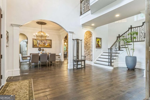entrance foyer featuring a towering ceiling, a chandelier, wood-type flooring, arched walkways, and ornate columns