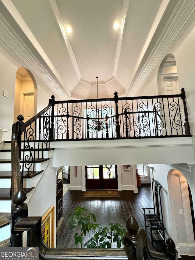 stairs featuring arched walkways, an inviting chandelier, wood-type flooring, and a tray ceiling