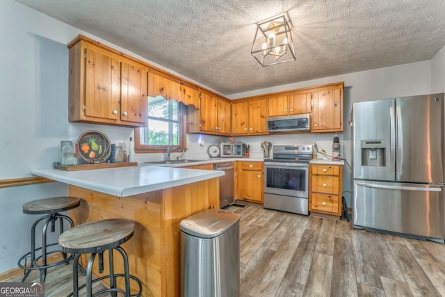 kitchen featuring light wood-style flooring, brown cabinetry, stainless steel appliances, a sink, and a peninsula