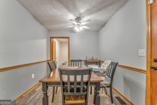 dining space featuring wood finished floors, ceiling fan, baseboards, visible vents, and a textured ceiling