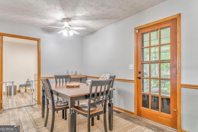 dining area with light wood-style floors, a ceiling fan, and a textured ceiling