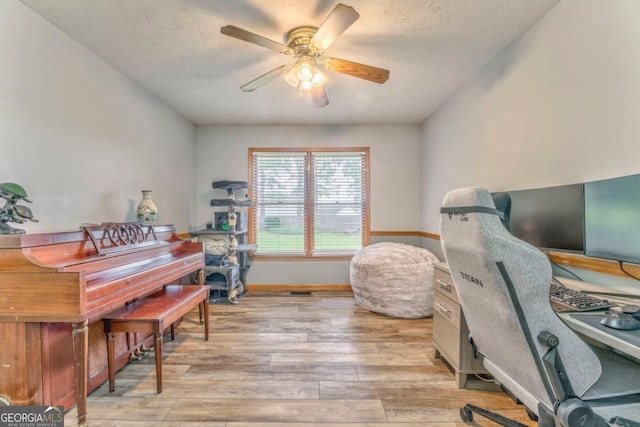 office space featuring baseboards, a ceiling fan, light wood-style floors, and a textured ceiling