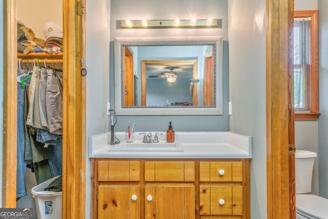 bathroom with toilet, ceiling fan, vanity, and a spacious closet
