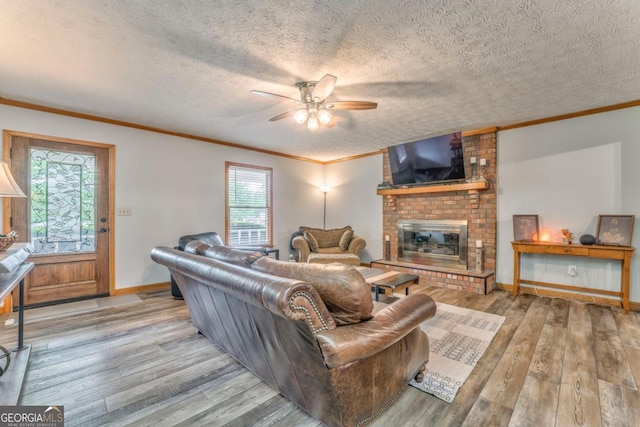 living area with a fireplace, wood finished floors, ceiling fan, and crown molding