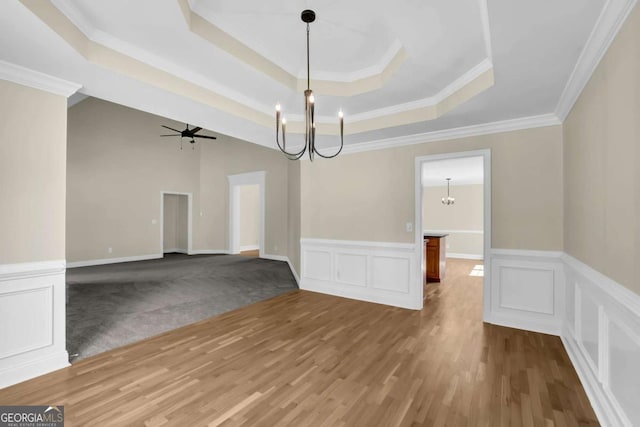 unfurnished dining area with a decorative wall, ceiling fan with notable chandelier, a wainscoted wall, wood finished floors, and a tray ceiling