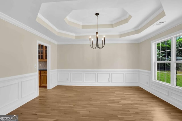 unfurnished dining area featuring visible vents, light wood-type flooring, a raised ceiling, an inviting chandelier, and ornamental molding