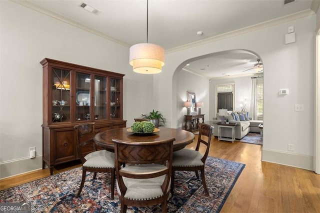 dining space with visible vents, a ceiling fan, crown molding, wood finished floors, and arched walkways