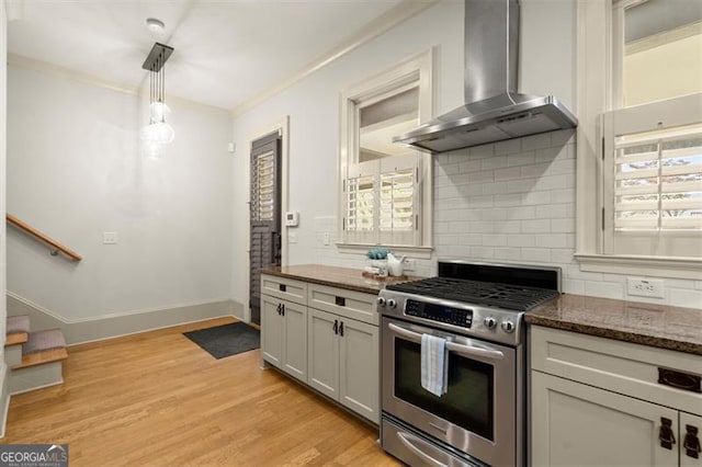 kitchen featuring hanging light fixtures, tasteful backsplash, gas stove, light wood finished floors, and wall chimney exhaust hood