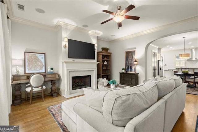 719 Hammond Dr, Woodstock, GA 30188 - living room featuring ceiling fan, arched walkways, light wood-style flooring, a fireplace, and crown molding