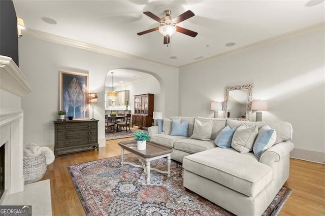living room featuring crown molding, arched walkways, ceiling fan, and wood finished floors