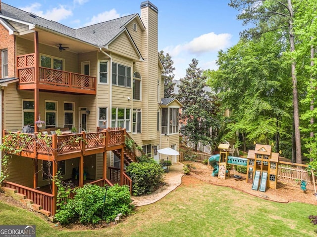 back of property with ceiling fan, a chimney, a lawn, a balcony, and a playground