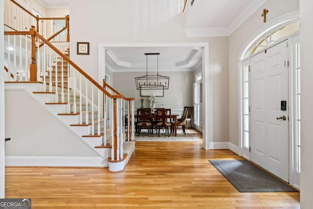 entryway with light wood-style floors, an inviting chandelier, stairs, and crown molding