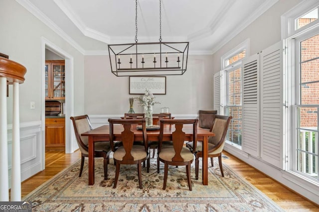 dining area with crown molding, an inviting chandelier, wainscoting, light wood-type flooring, and a raised ceiling