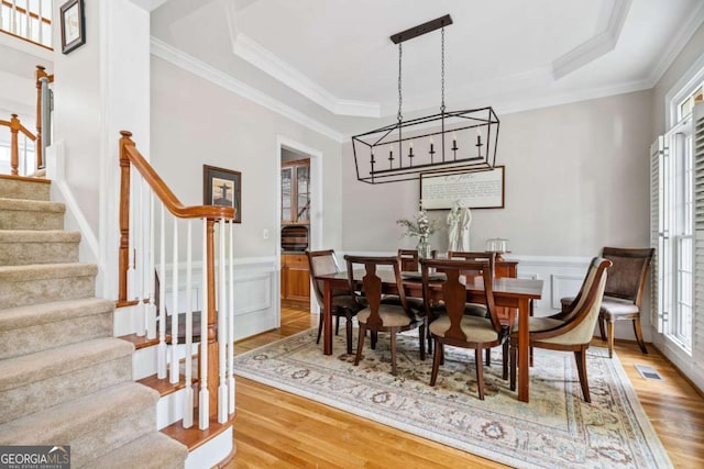dining room with crown molding, a raised ceiling, stairway, and light wood-type flooring