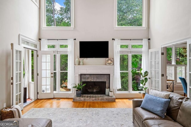 living area with french doors, a high ceiling, a fireplace, and wood finished floors