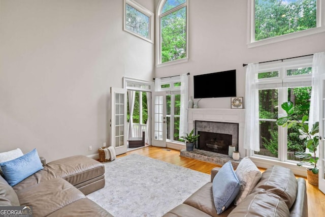 living area with wood finished floors, a brick fireplace, a high ceiling, and a wealth of natural light