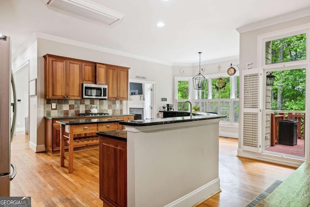 kitchen featuring decorative backsplash, brown cabinetry, stainless steel appliances, light wood-style flooring, and an island with sink