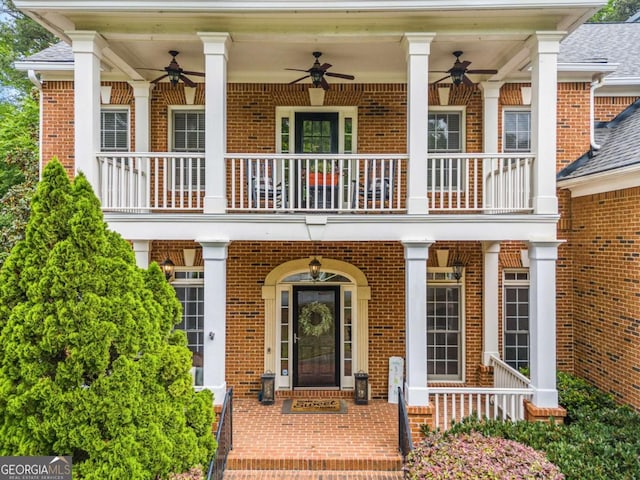 entrance to property featuring brick siding, ceiling fan, and a balcony