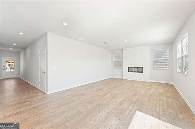 unfurnished living room featuring baseboards, recessed lighting, light wood-style flooring, and a glass covered fireplace