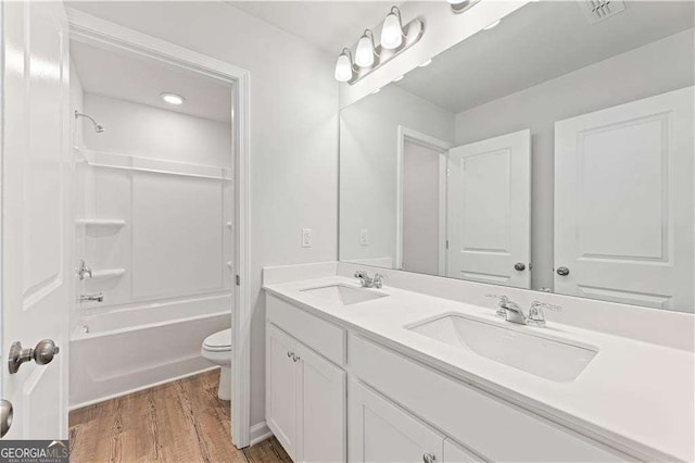 bathroom with toilet, double vanity, a sink, and wood finished floors