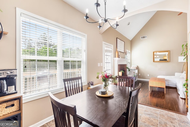 dining area featuring a brick fireplace, baseboards, visible vents, a notable chandelier, and high vaulted ceiling