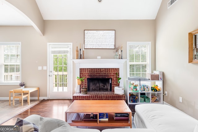 living room with a fireplace, visible vents, baseboards, arched walkways, and wood finished floors
