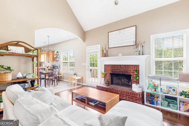 living room featuring a chandelier, high vaulted ceiling, wood finished floors, and a brick fireplace