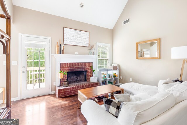 living area featuring wood finished floors, visible vents, high vaulted ceiling, and a brick fireplace
