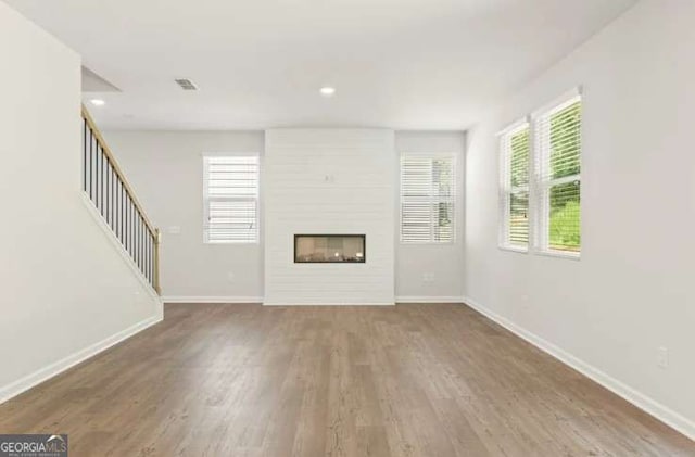 unfurnished living room featuring a large fireplace, wood finished floors, and baseboards