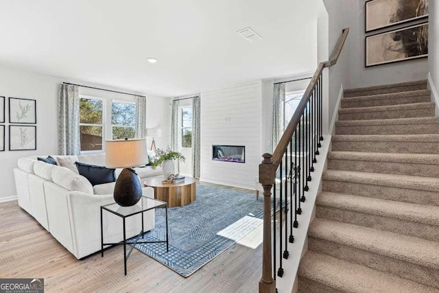 living area featuring visible vents, stairway, a large fireplace, baseboards, and light wood-type flooring