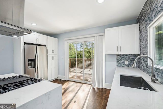 kitchen with light stone countertops, stainless steel fridge, a sink, white cabinetry, and baseboards