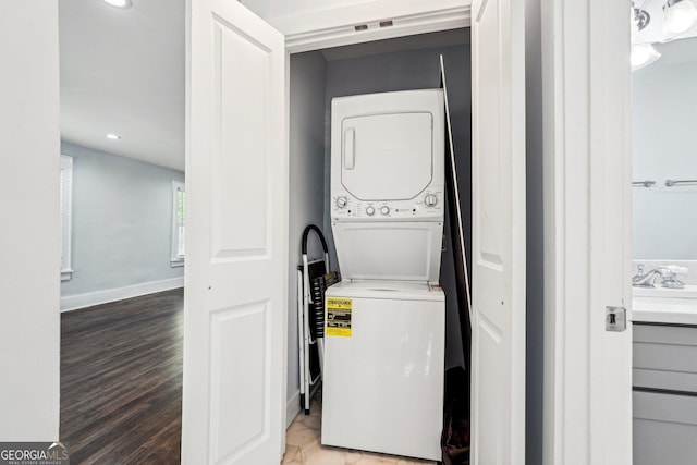 laundry room featuring laundry area, stacked washer / drying machine, recessed lighting, baseboards, and wood finished floors